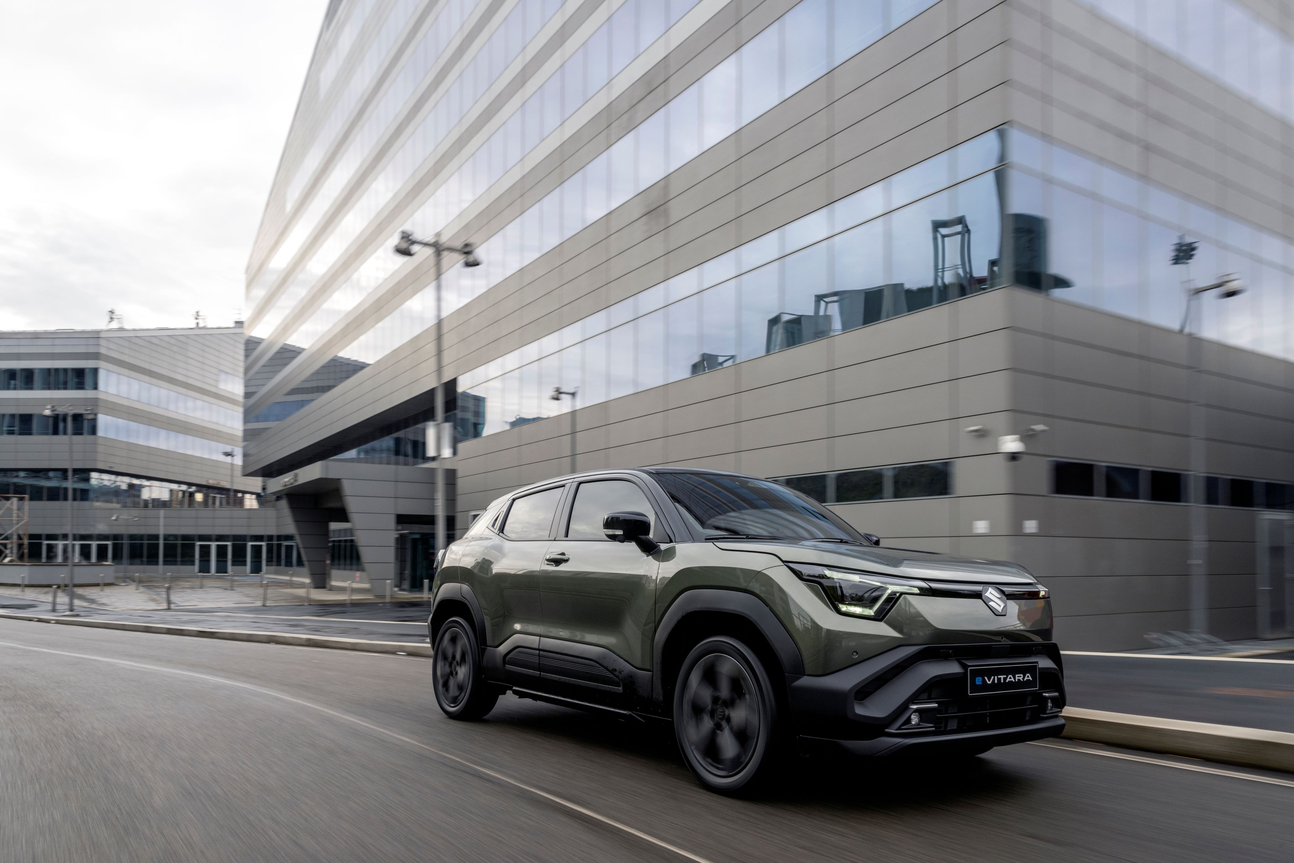 Green SUV driving past modern glass buildings.