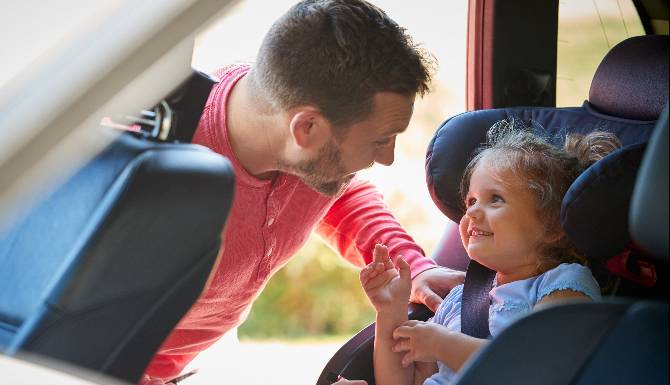 Father Securing Daughter Into Car Seat