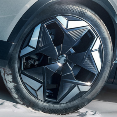 Close-up of a car wheel with a geometric alloy design on a snowy surface.