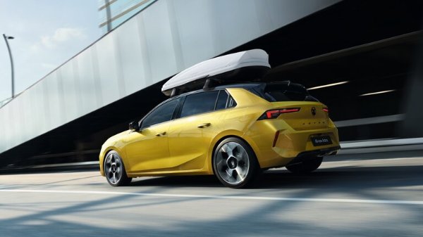 Yellow hatchback car with a roof box driving in an urban setting.