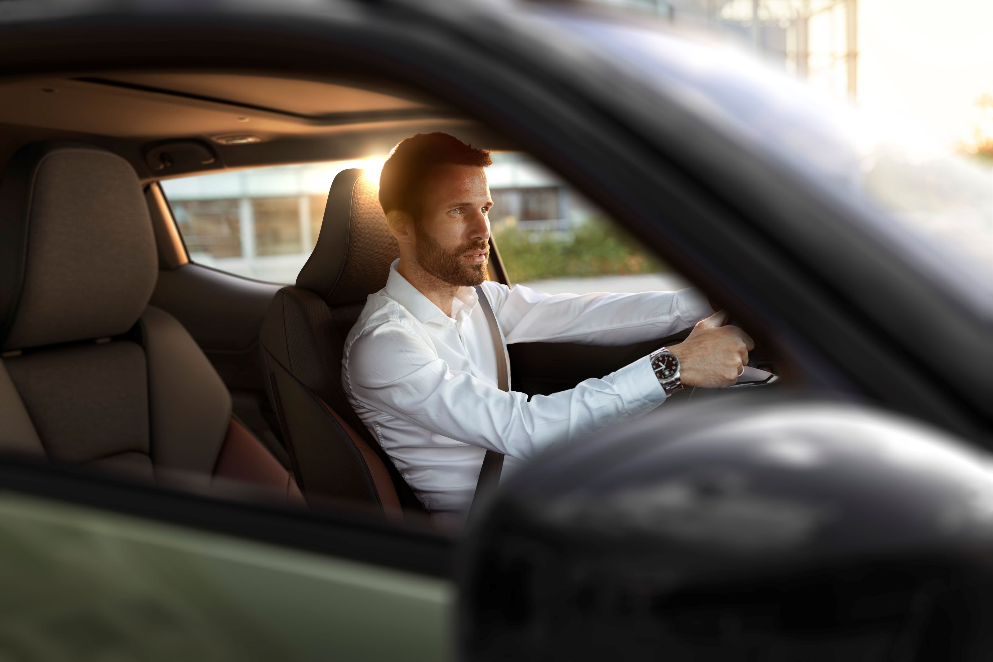 Man in a white shirt driving a car, with sunlight through the window.