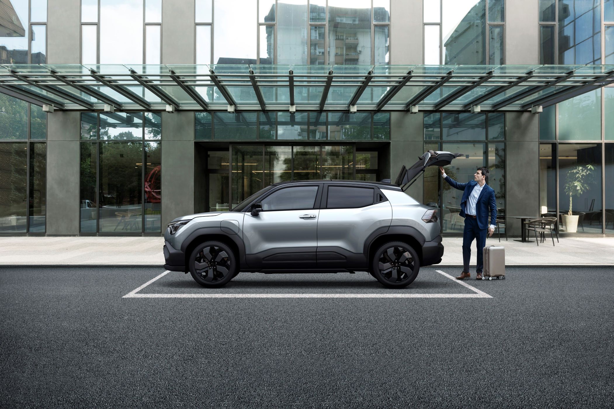 Man in suit loading suitcase into silver SUV with raised boot.